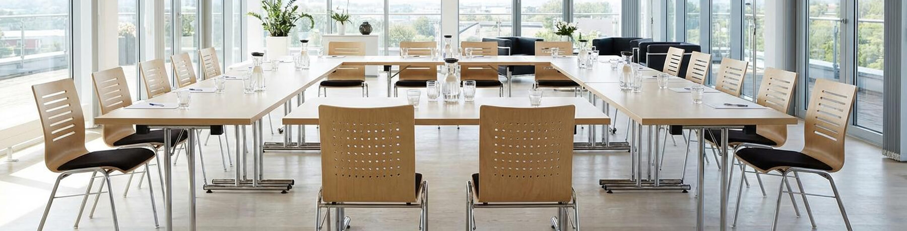Heller, moderner Konferenzraum mit U-förmig angeordneten Tischen und stapelbaren Holzstühlen – professionelle Konferenzmöbel für Meetings und Seminare.